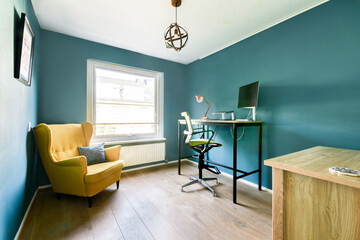 A stylish and contemporary office corner featuring a green accent wall, a cozy armchair, and a sleek desk with a computer, creating an inviting work environment.