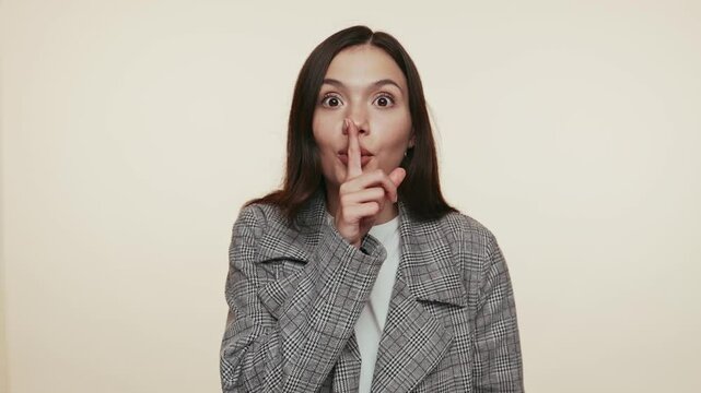 A young woman in a plaid jacket making a shushing gesture, implying a secret or a request for silence.