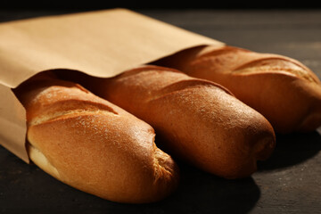 Paper bag with fresh baguettes on black wooden table, closeup
