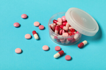 Jar with different pink pills on blue background, closeup