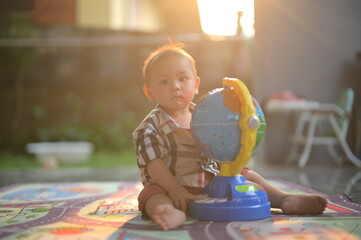 A young child plays with a colorful globe toy on a patterned mat, basking in warm sunlight, conveying a sense of curiosity and exploration.