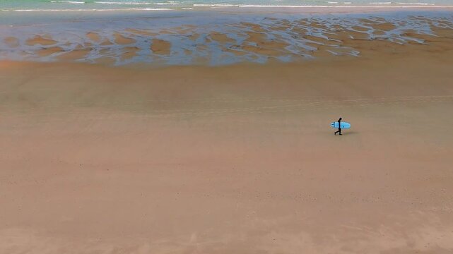 Surfeur en combinaison hiver marchant sur la plage - Planche sous le bras 