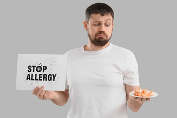 Young man holding paper with text STOP ALLERGY and shrimps on light background