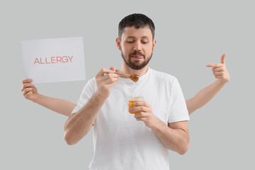 Young man with honey and female hands holding word ALLERGY on light background