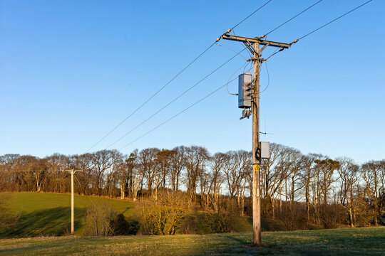 Wooden Electricity Utility Pole with Overhead Power Lines and Transformers in a Field Against a Clear Blue Sky