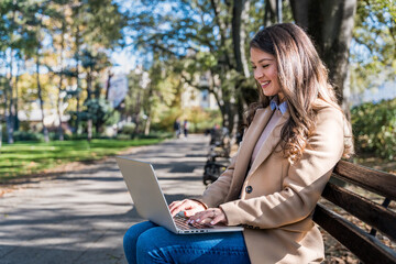 Successful businesswoman, office worker in corporate business, sitting on park bench working on laptop computer. Dedicated independent strong CEO female end of working time, finishing work outside.