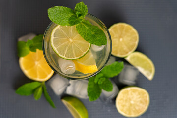 Glass of lemonade with lemon and mint, lime and on a dark background with scattered ice and citrus...