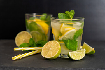 Two lemon and mint drinks with lemongrass and straws for the drink on a dark surface. Soft focus on...