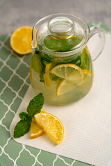 Citrus detox tea in a teapot with lemon and mint on a light background. Refreshing summer drinks. Food photo for catalog, publications, magazines.