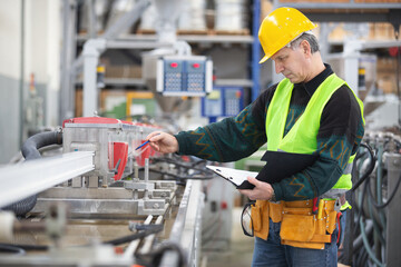 Senior worker in the factory operating machines and taking notes