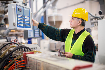 Senior worker in the factory operating machines and taking notes