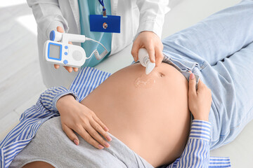 Lying pregnant woman and doctor with fetal doppler listening to baby's heartbeat in clinic, closeup