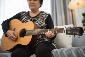 Obraz premium Older woman playing acoustic guitar at home showcasing passion for music and creativity, with comfortable living space as background setting