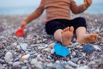 Toddler plays with bright toys on a pebbly beach during sunny afternoon