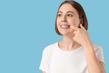 Young woman showing teeth with dental braces on blue background, closeup