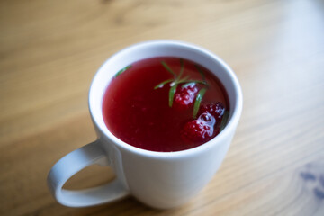 Raspberry tea in a white mug on a wooden table.