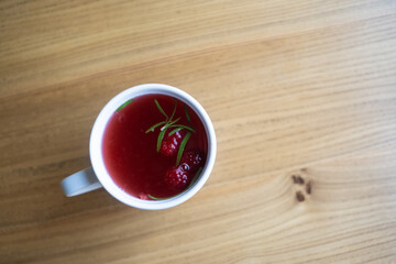 Raspberry tea in a white mug on a wooden table.