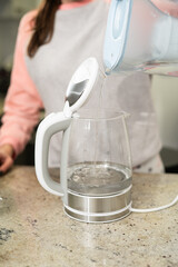 The filter jug is filled with purified water into a modern glass electric kettle.