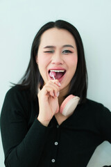 Young Asian woman smiling and winking while holding a cotton swab, showcasing playful energy in a...