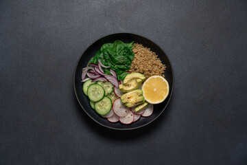 Quinoa, spinach, avocado, radish and lemon wedge vegan food. Healthy food in a bowl on a black background with copy space.