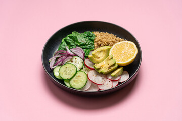 Quinoa, spinach, avocado, radish and lemon wedge vegan food. Healthy food in a bowl on a pink background with copy space.