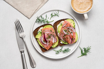 Smoked salmon avocado sandwich on light background. Black whole grain bread, avocado, salted salmon and dill for healthy breakfast