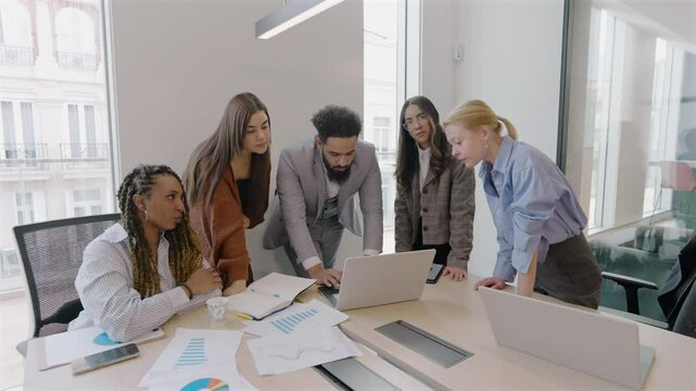 A group of diverse and skilled professionals gathered together, engaging in a vibrant collaborative discussion around a laptop situated in a bright and modern office space that fosters creativity
