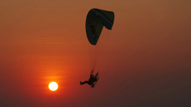 Motor paraglider flying through colorful sunset sky