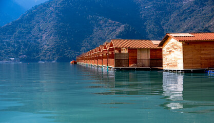 Floating huts in the lake are surrounded by a stunning blue mountain backdrop, often shrouded in a...