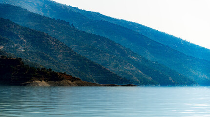 Obraz premium Multi-layered blue mountains rise majestically over the tranquil lake. The serene landscape creates a peaceful atmosphere for visitors.