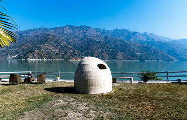 A dome sofa provides a cozy spot for relaxing in the lawn, overlooking a serene lake. A palm tree on the side adds to the tropical ambiance.