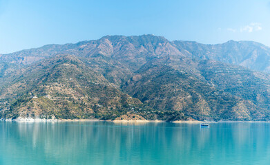 A tranquil lake is framed by tall mountains on the other side. A floating boat adds a touch of adventure to the peaceful scenery.