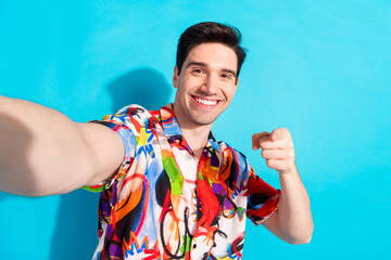 Portrait of a cheerful young man in a vibrant shirt posing enthusiastically against a bright blue...