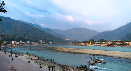 A wide view of Rishikesh town displays both sides of the river Ganges. The vibrant town life is complemented by the natural beauty surrounding it.
