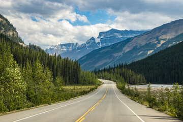 Scenic winding road through mountains and forests on a clear day with soft clouds