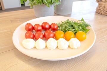Fresh caprese salad ingredients with red cherry tomatoes, yellow tomatoes, mozzarella, and arugula on plate