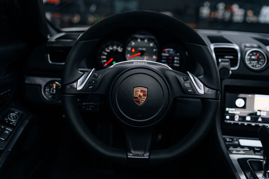 Close-up of Porsche Boxster S steering wheel &ndash; leather-wrapped sports design with Porsche crest, paddle shifters, and PDK emblem in luxury black interior cockpit lighting