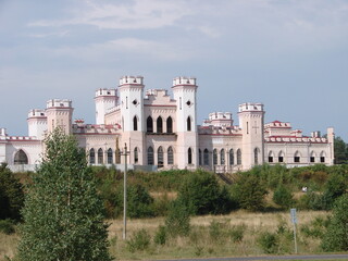 Fototapeta premium Historic Puslovsky Palace with neo-Gothic architecture, white facade and red roofs, surrounded by greenery under a clear summer sky