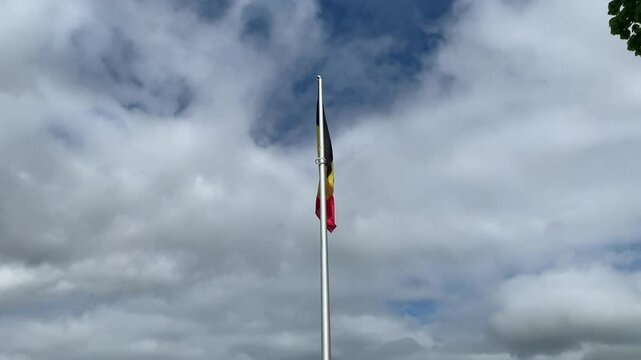 Belgian flag is waving on a metal pole. Bright sky with white clouds. Flag is placed next to Saint Donat church at Arlon city centre