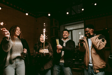 Friends celebrating birthday with cake and sparklers in cozy indoor setting during evening gathering
