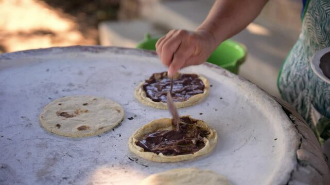 Cook preparing traditional mexican food on comal with cheese and beans