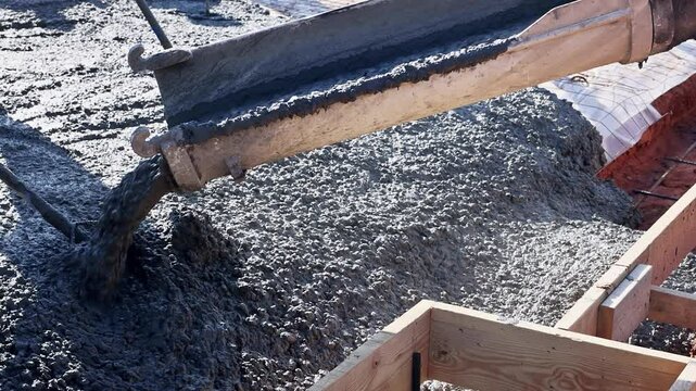 Workers pour fresh concrete foundation slab into wooden forms at construction site