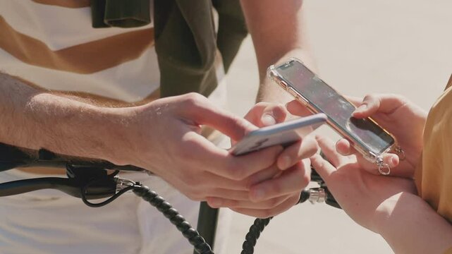 Close camera view of two people holding smartphones while standing near scooter outdoors. Comparing maps or exchanging contacts. Showing each other something important or coordinating next step.