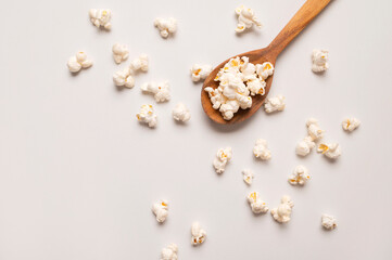 White salty or sweet popcorn in wooden spoon on light gray background top view. Scattered cornflakes, food for movie or cinema. Tasty snack, party snack