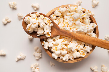 White salty or sweet popcorn in wooden spoon on light gray background top view. Scattered cornflakes, food for movie or cinema. Tasty snack, party snack