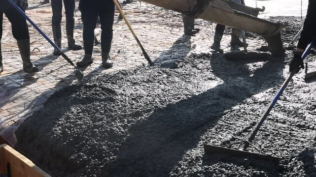Construction workers are collaborating to pour fresh concrete slab into molds at building site