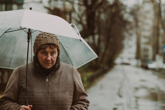 Thoughtful woman holding a transparent umbrella on a rainy day in an urban environment while contemplating life