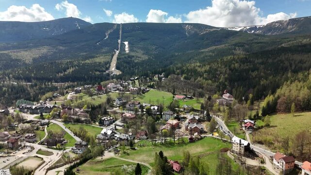 Aerial spring view of Karpacz, Poland &mdash; a picturesque mountain town nestled in the Karkonosze Mountains, surrounded by lush forests, scattered snow patches, and charming traditional houses.