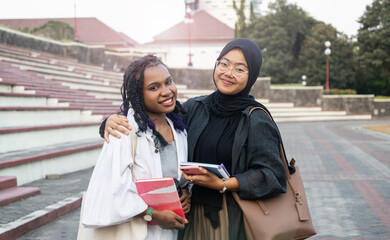 Two multi-ethnic female students hugging on campus, showing diversity and friendship, muslim and Asian