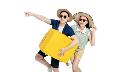 portrait of asian couple wearing travel clothes, carrying suitcases and posing on white background